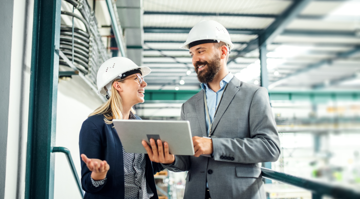 Two employees in hard hats looking at a tablet.